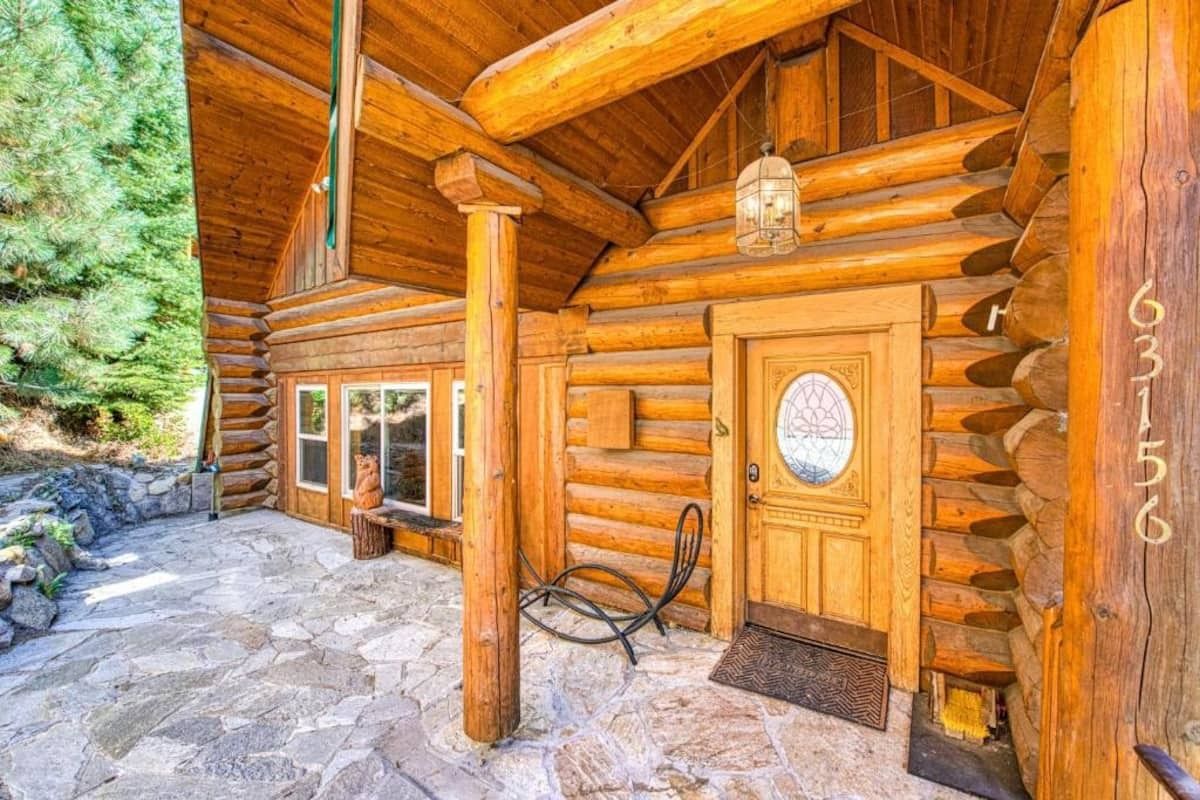 Rustic log cabin porch with wooden pillars, stone floor, and a front door under a covered entryway