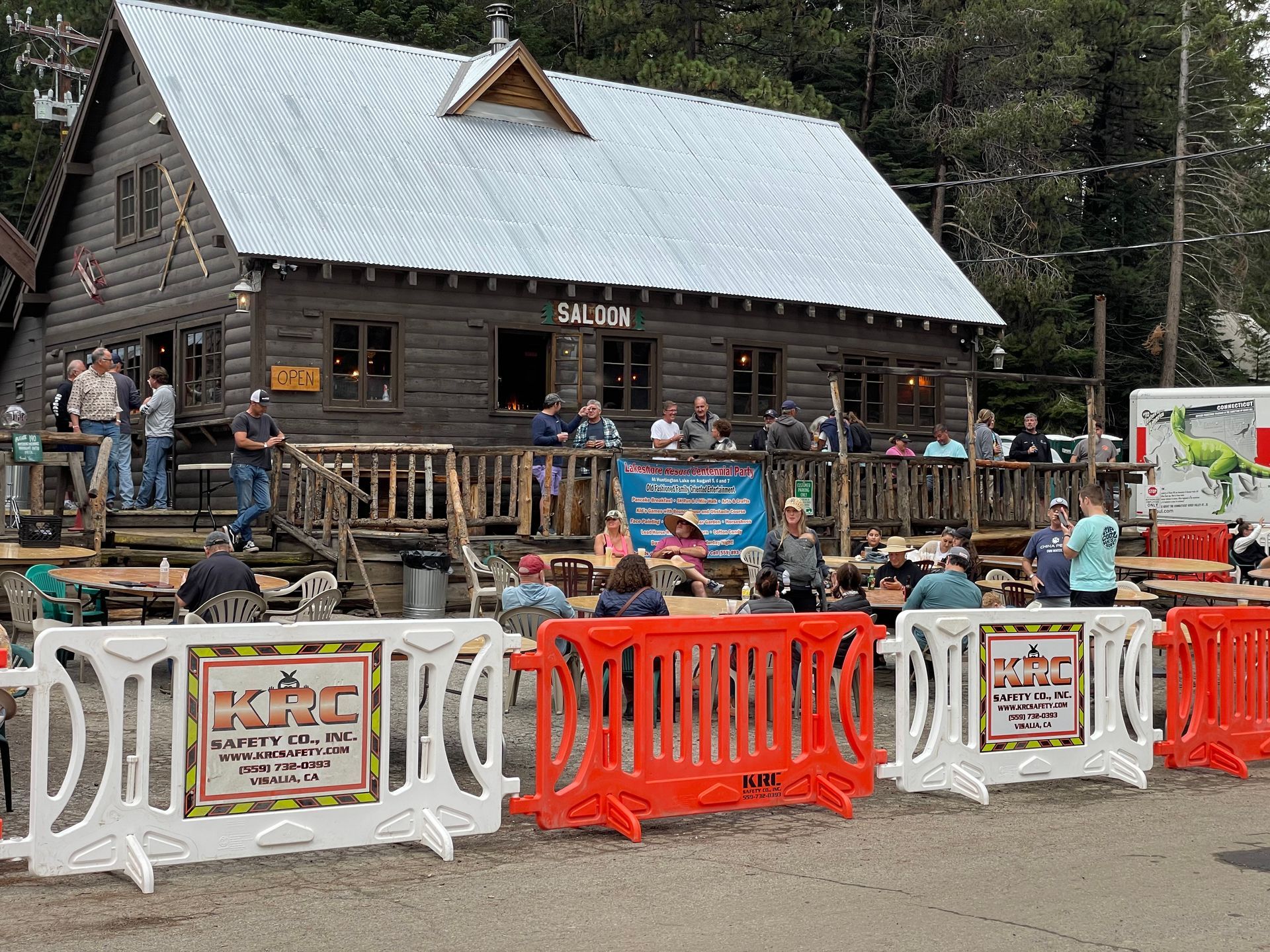 People gathered outside a log cabin with a porch and orange-and-white barricades in front