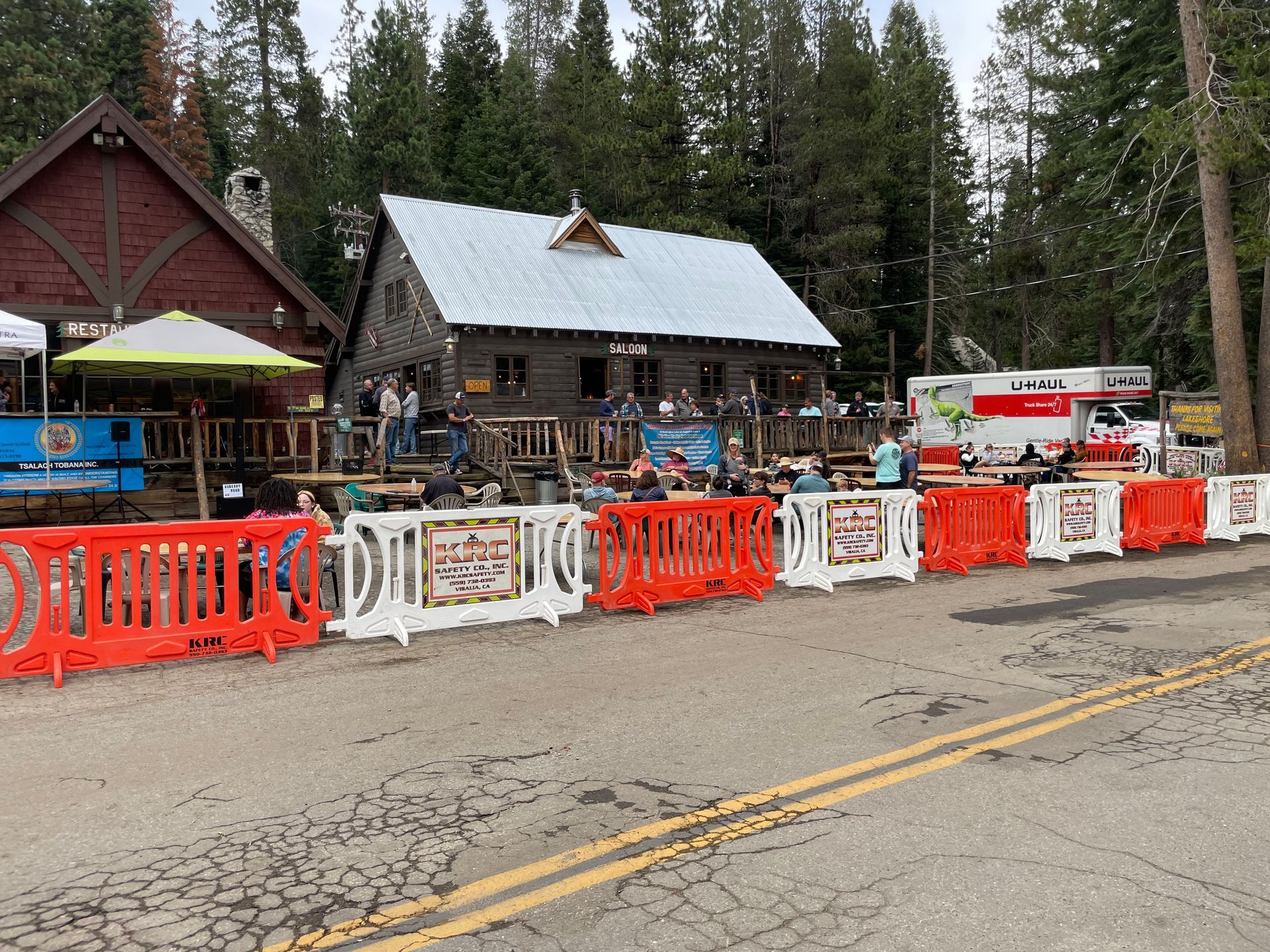 Street-side cabins with red-and-white barriers, parked bikes, and a red bus in a forested area