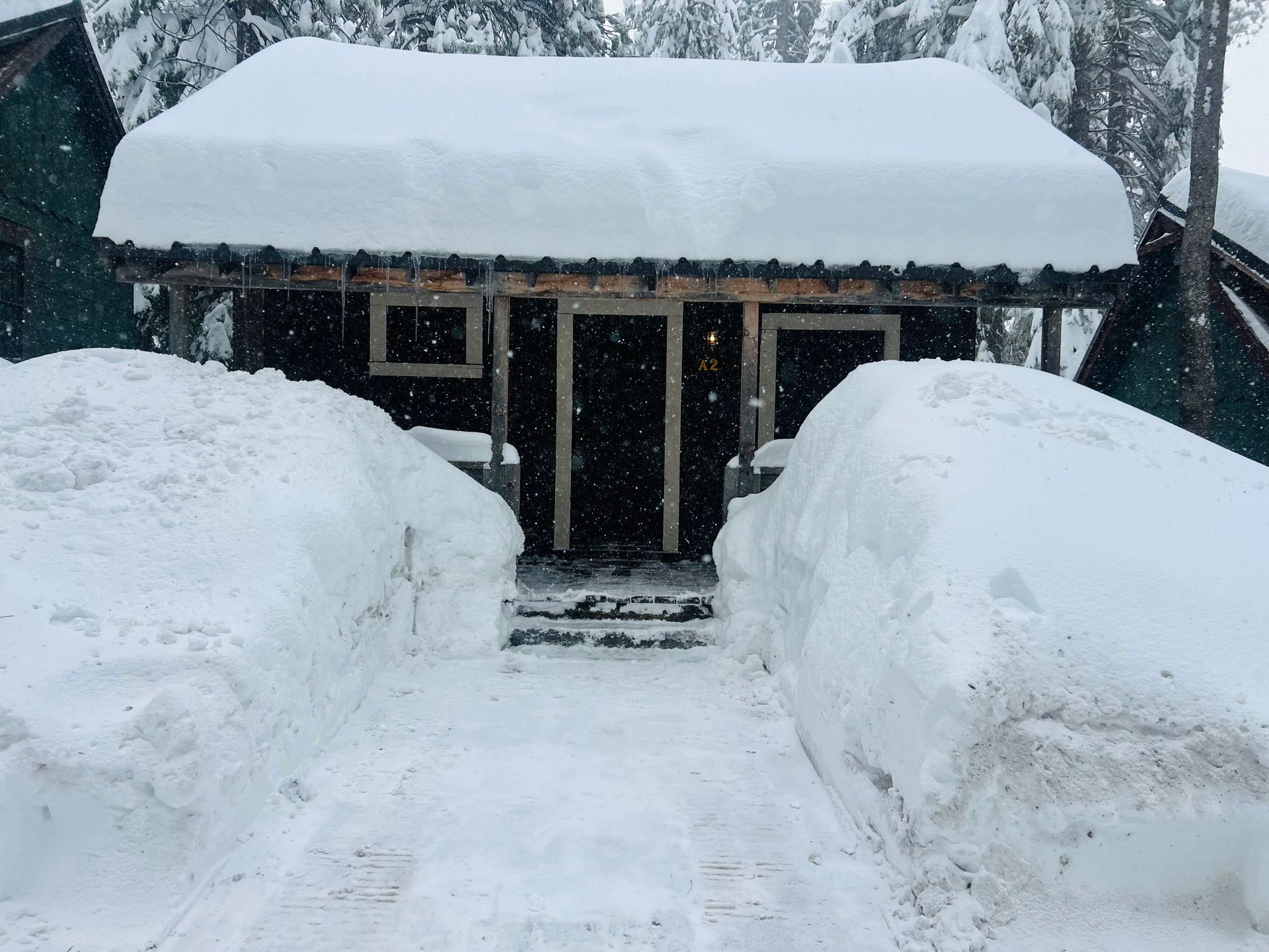 Snowy cabin with a cleared path between tall snowbanks and a snow-covered roof