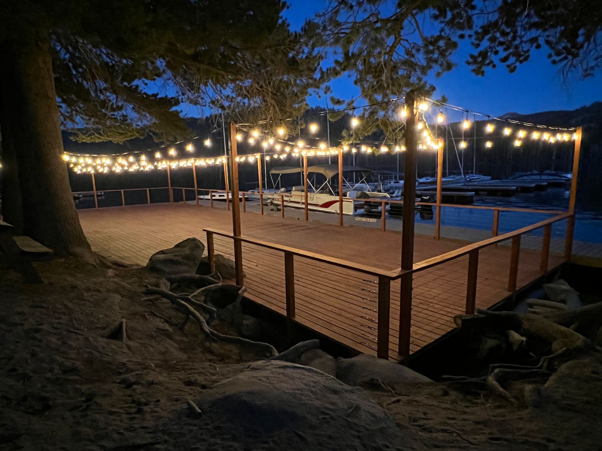 Lit outdoor deck with string lights and lounge chairs by a pool at dusk