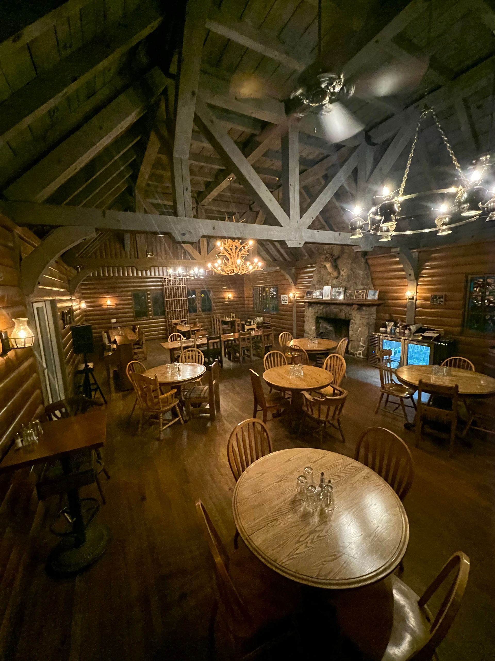 Rustic cabin reception hall with long tables set for a celebration, decorated with greenery and string lights.