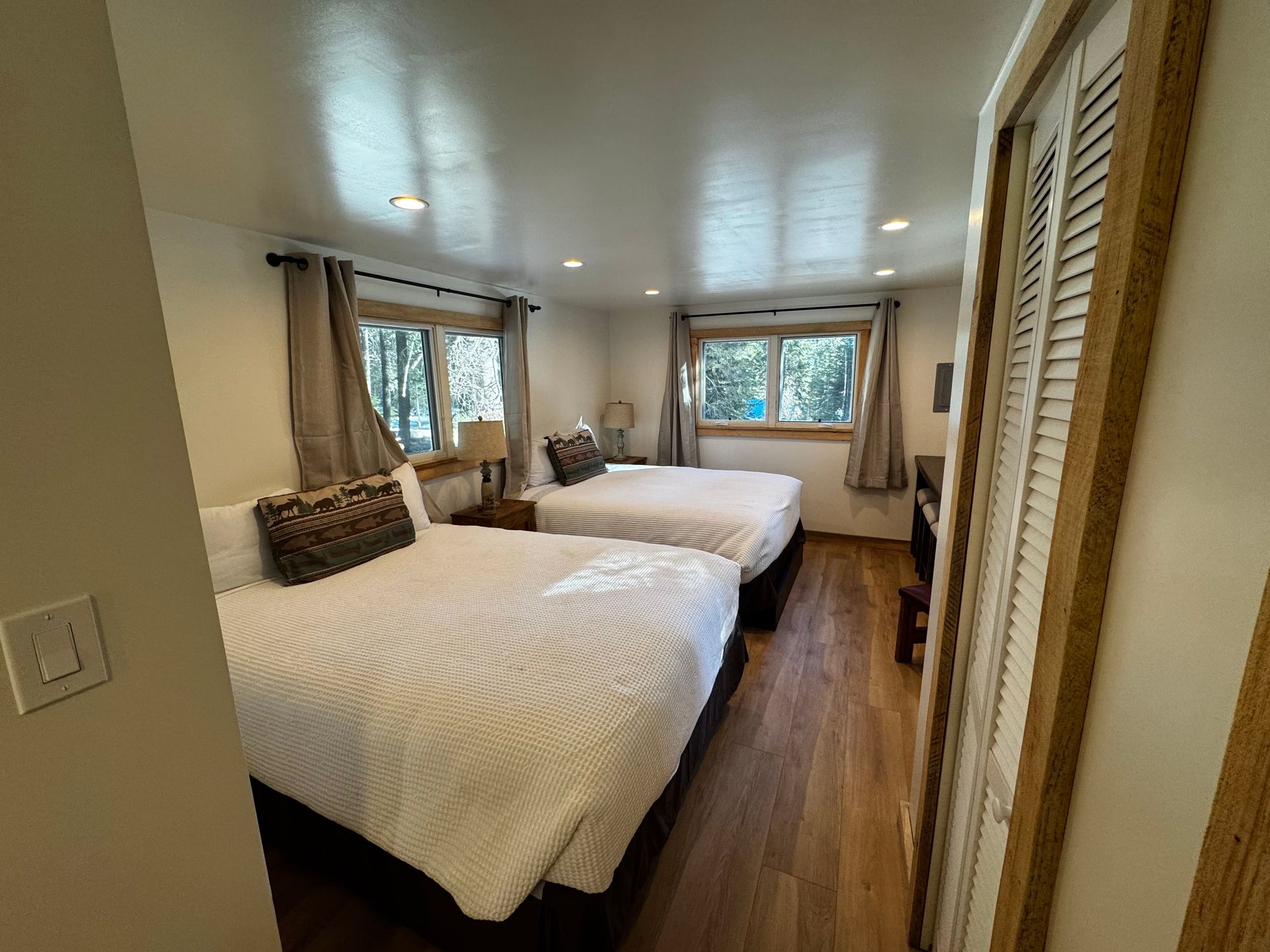 Bright bedroom with two white beds, wood floors, and windows with curtains