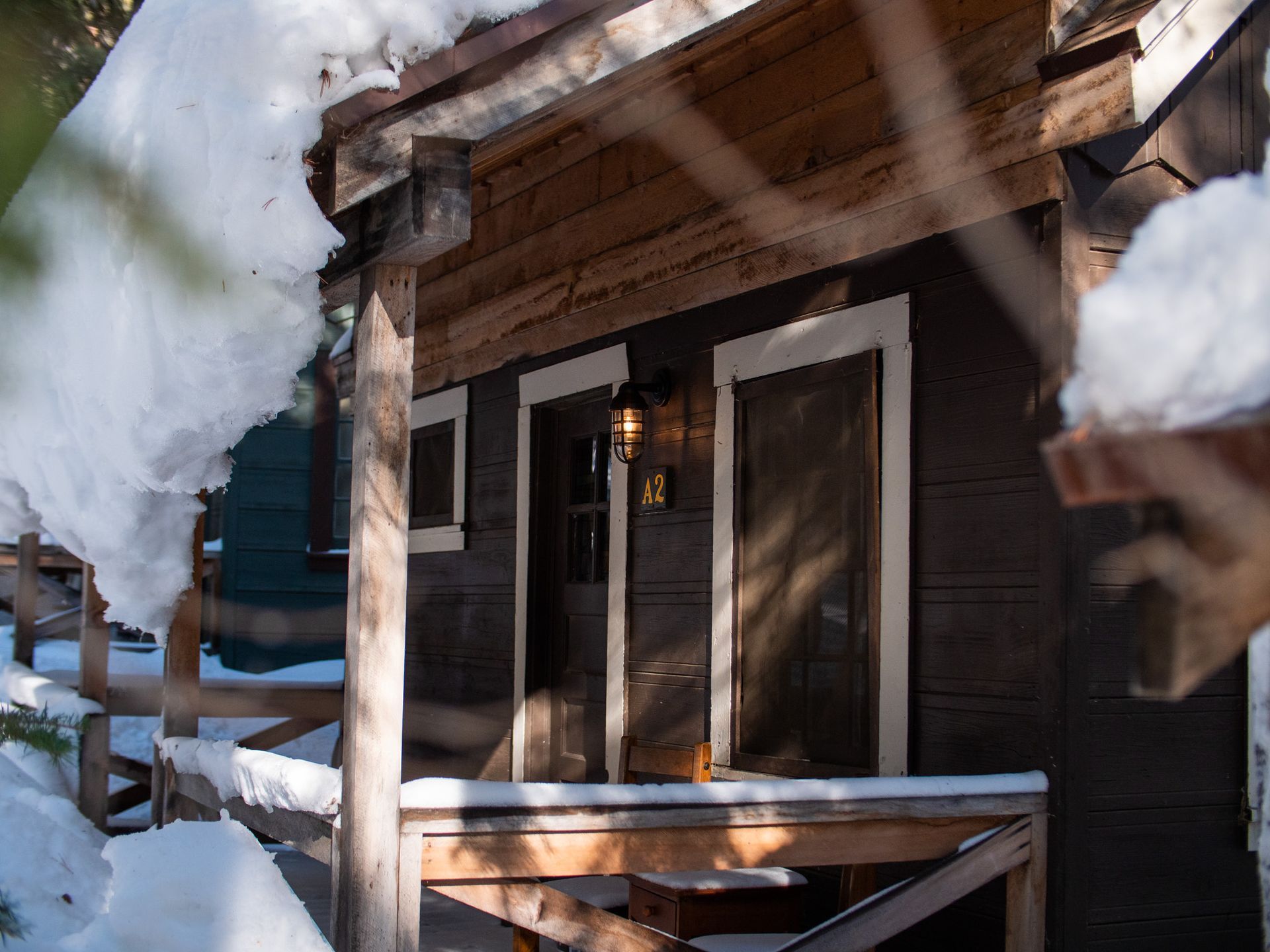 Snow-covered cabin porch with wooden railings and a lantern by the front door