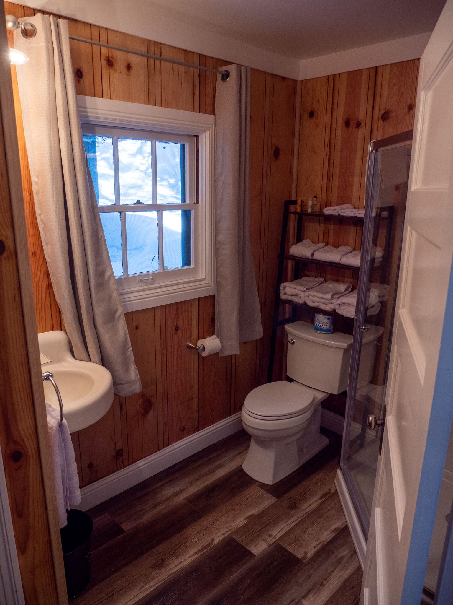 Small wood-paneled bathroom with toilet, window, sink, and shower curtain.