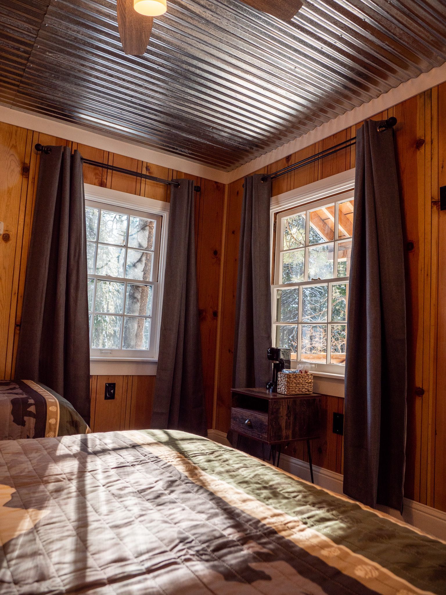 Cozy wood-paneled bedroom with two windows, a bed, and sunlight on the blanket