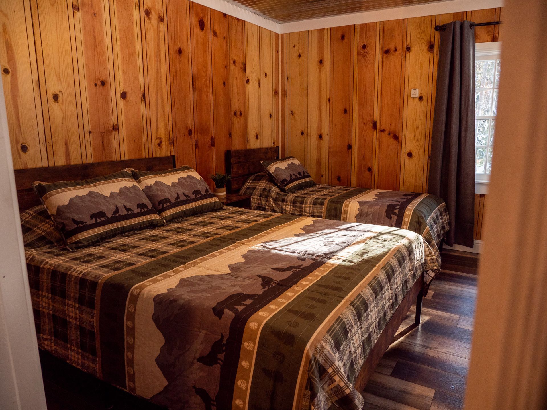 Cozy wood-paneled bedroom with a large bed, plaid bedding, and a window with curtains