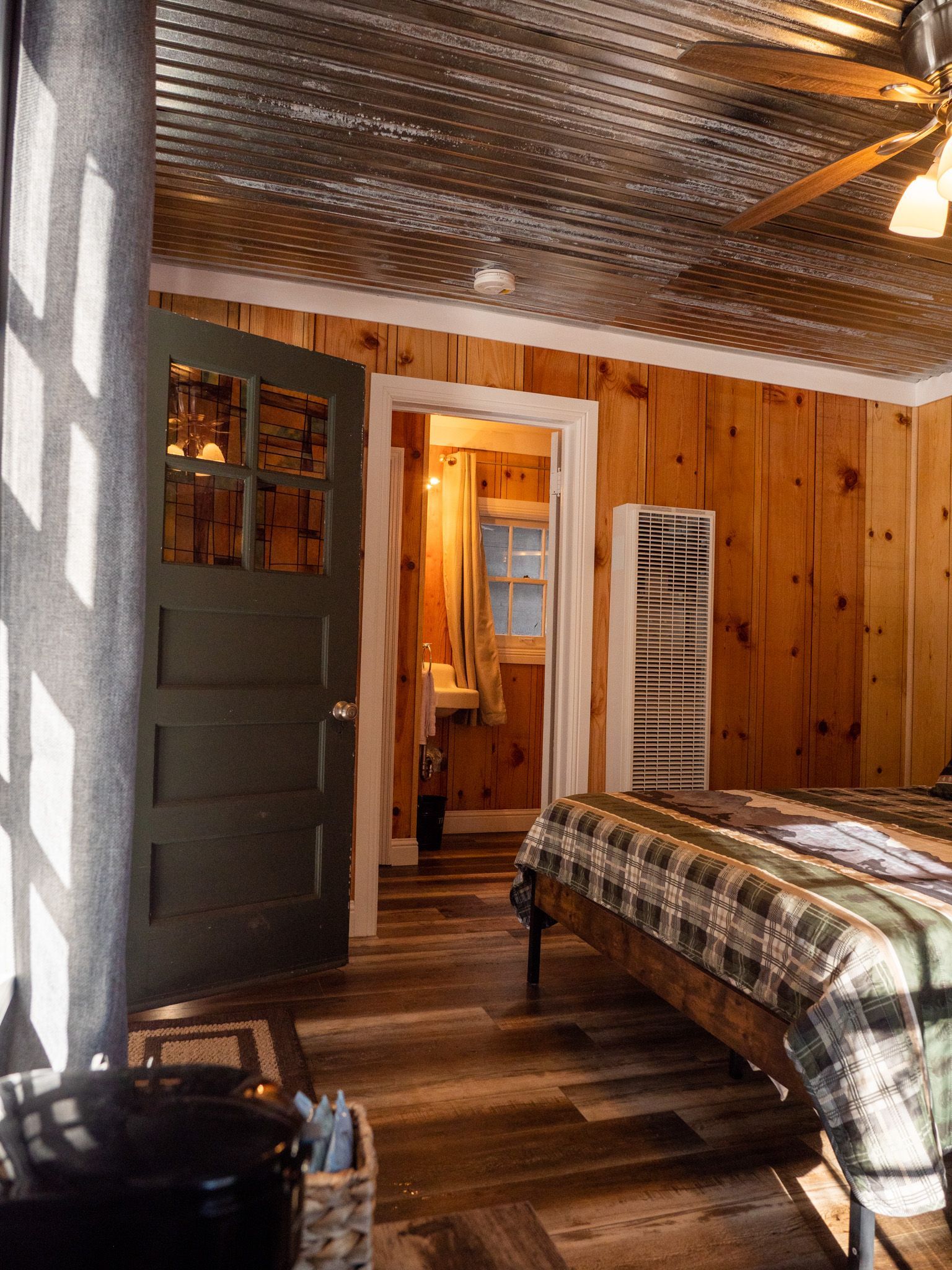 Cozy bedroom with wood-paneled walls, a metal bed, open door, and patterned ceiling fan