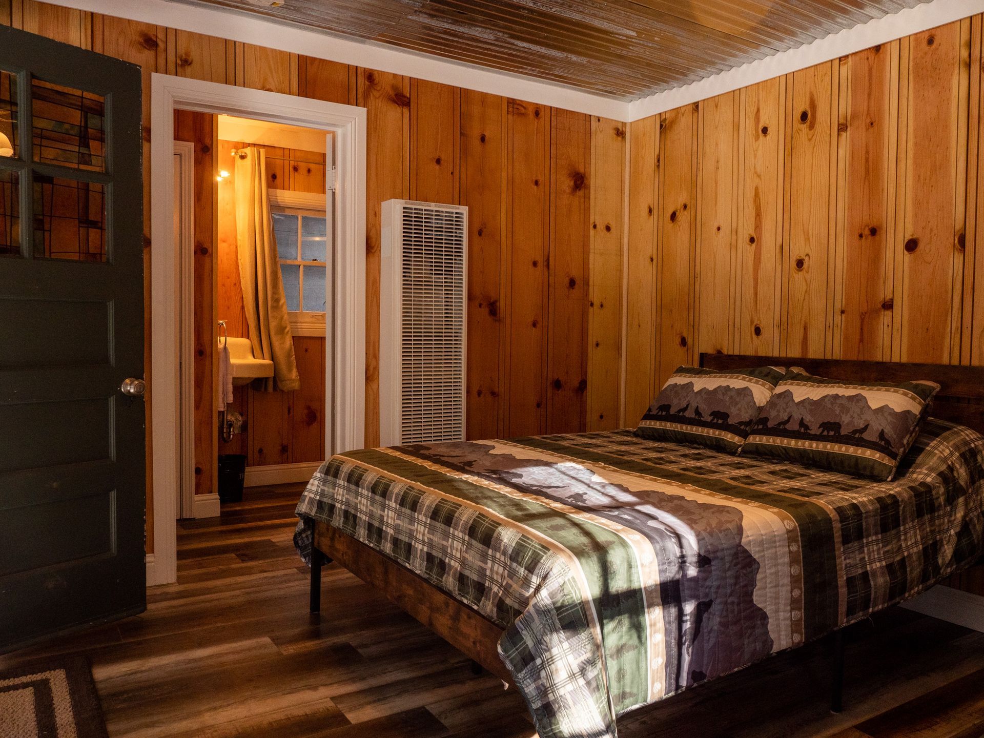 Cozy wooden bedroom with a bed, dresser, and warm lighting, seen through an open doorway