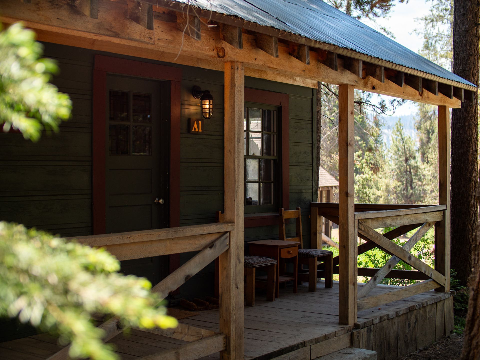 Rustic cabin porch with wooden railing, dark green door, and warm light in a forest setting