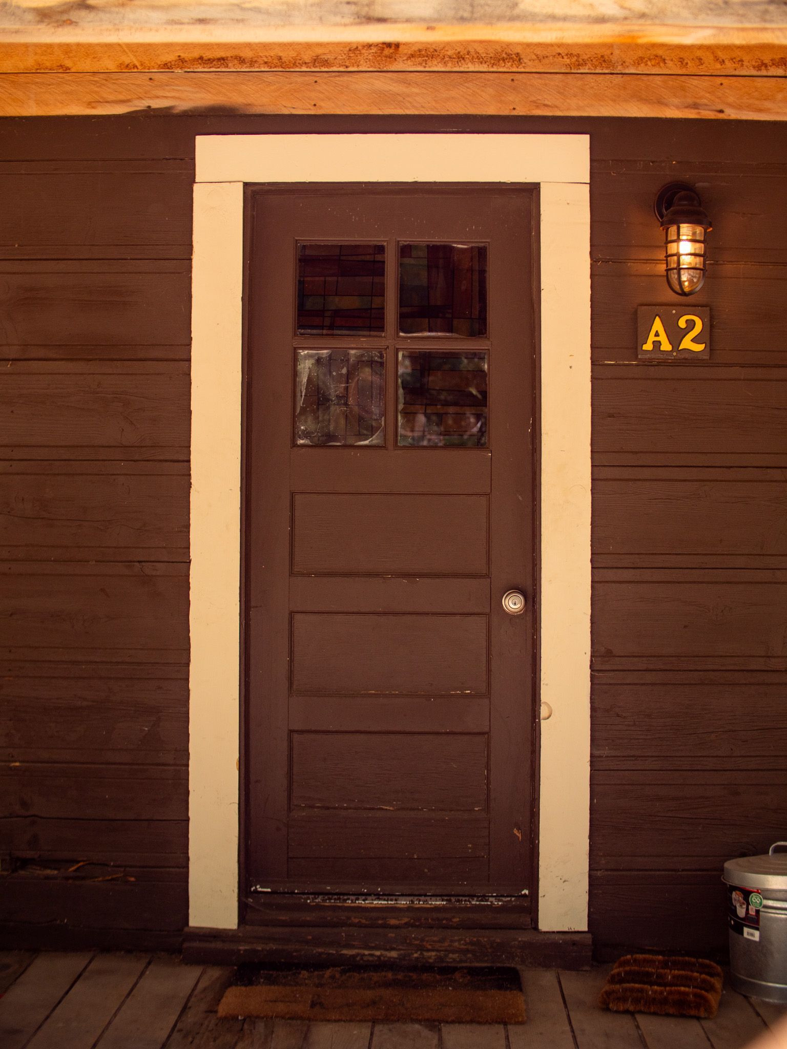Dark brown wooden door with white trim on a wooden wall, lit by a wall lantern and marked “A2.”
