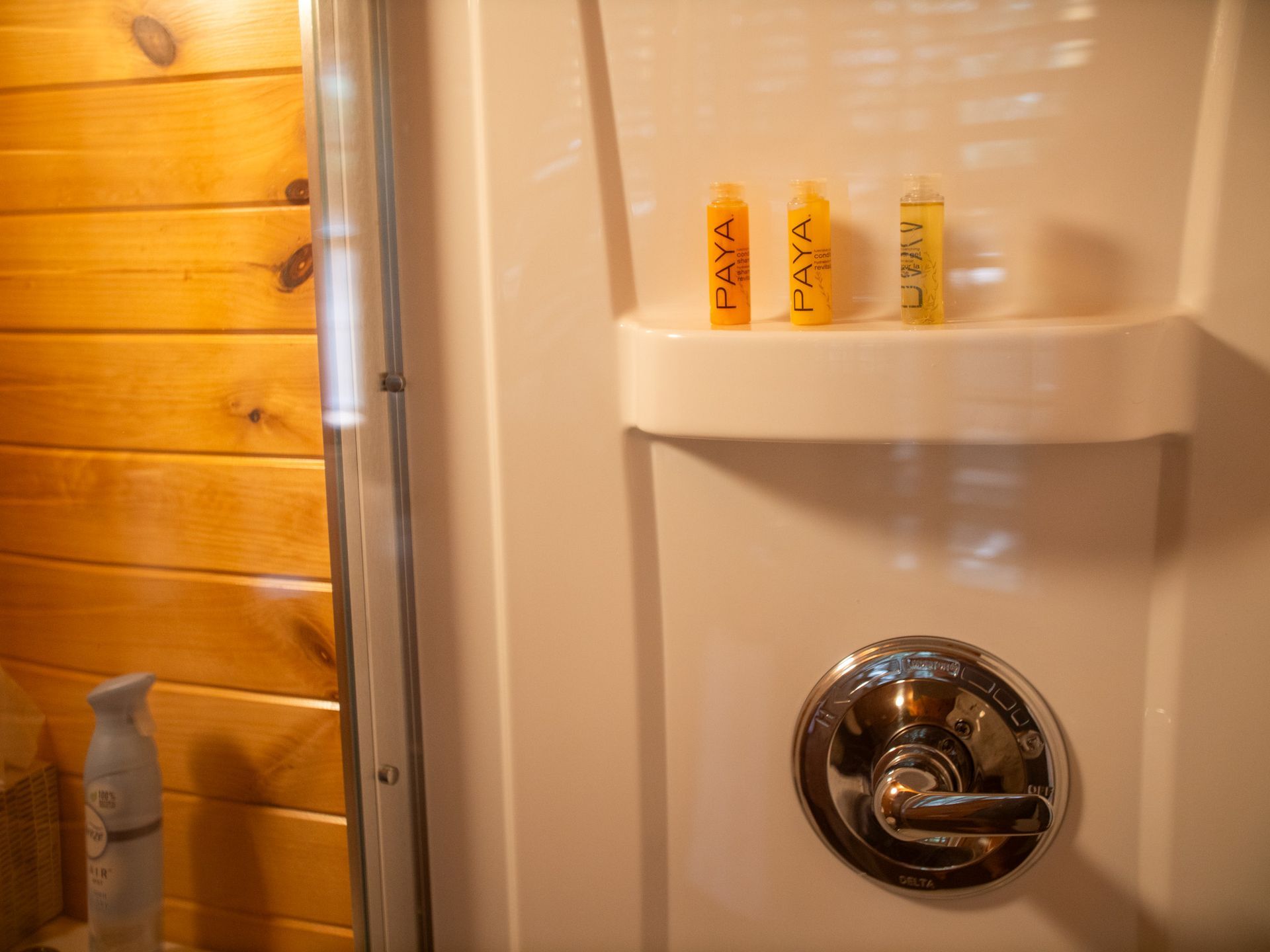 Bathroom shower with built-in shelf holding three small bottles beside a wooden wall