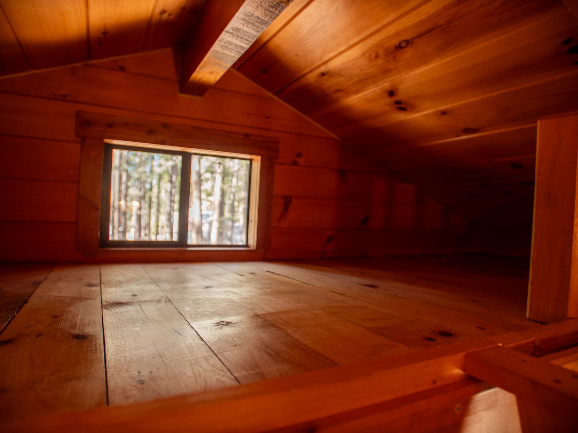 Empty wooden attic room with a small window and slanted ceiling, lit by warm natural light