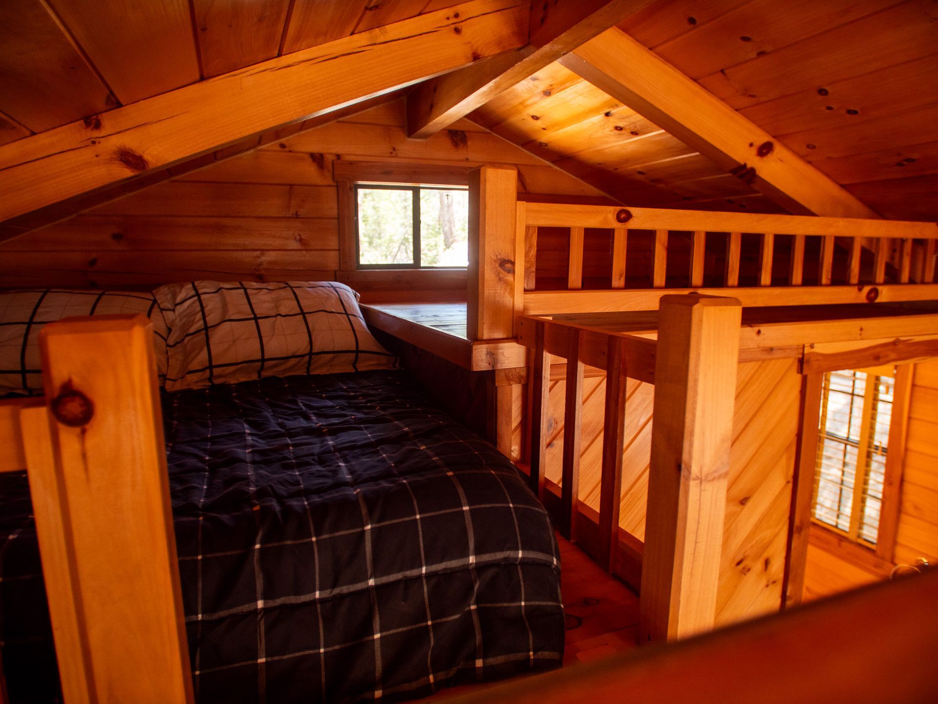 Cozy wooden loft bedroom with a bed, railing, and small window under slanted beams