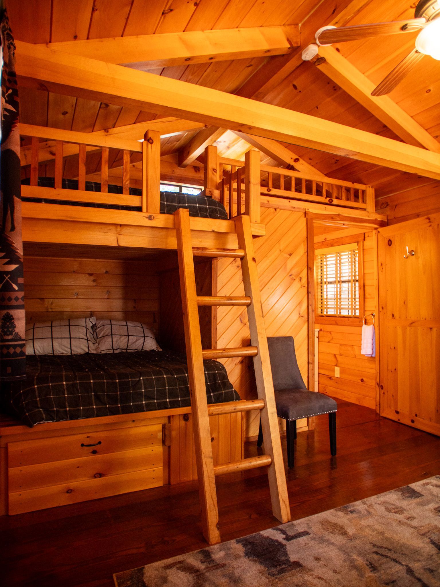 Cozy wooden cabin loft with ladder, bunk bed, and chair in warm orange light