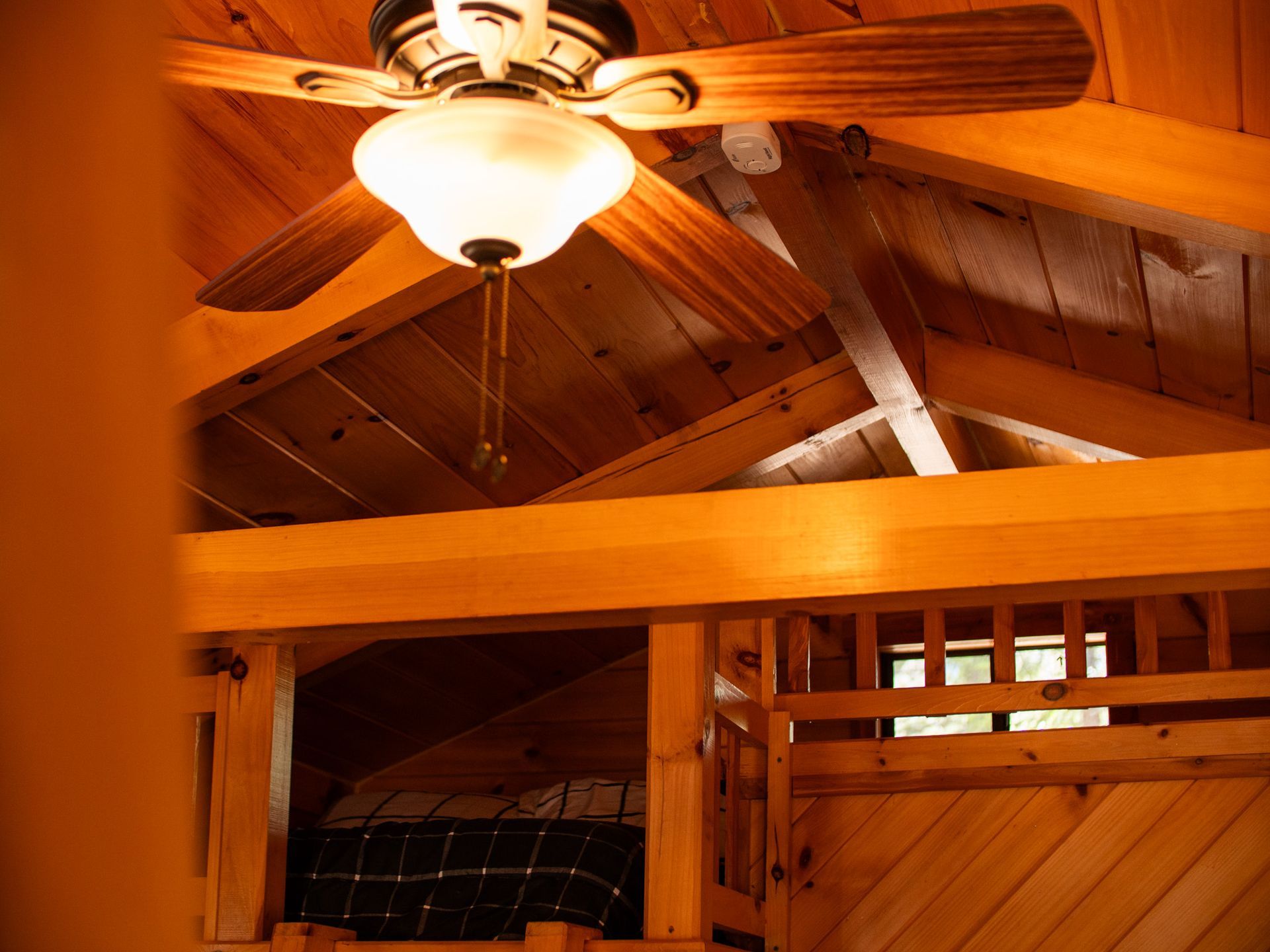 Wood-paneled attic room with vaulted ceiling, ceiling fan, and warm overhead light
