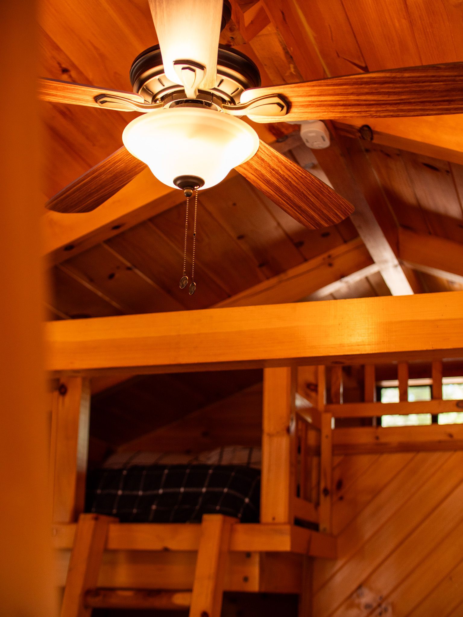 Wooden bunk loft interior with ceiling fan and warm lighting, viewed from below
