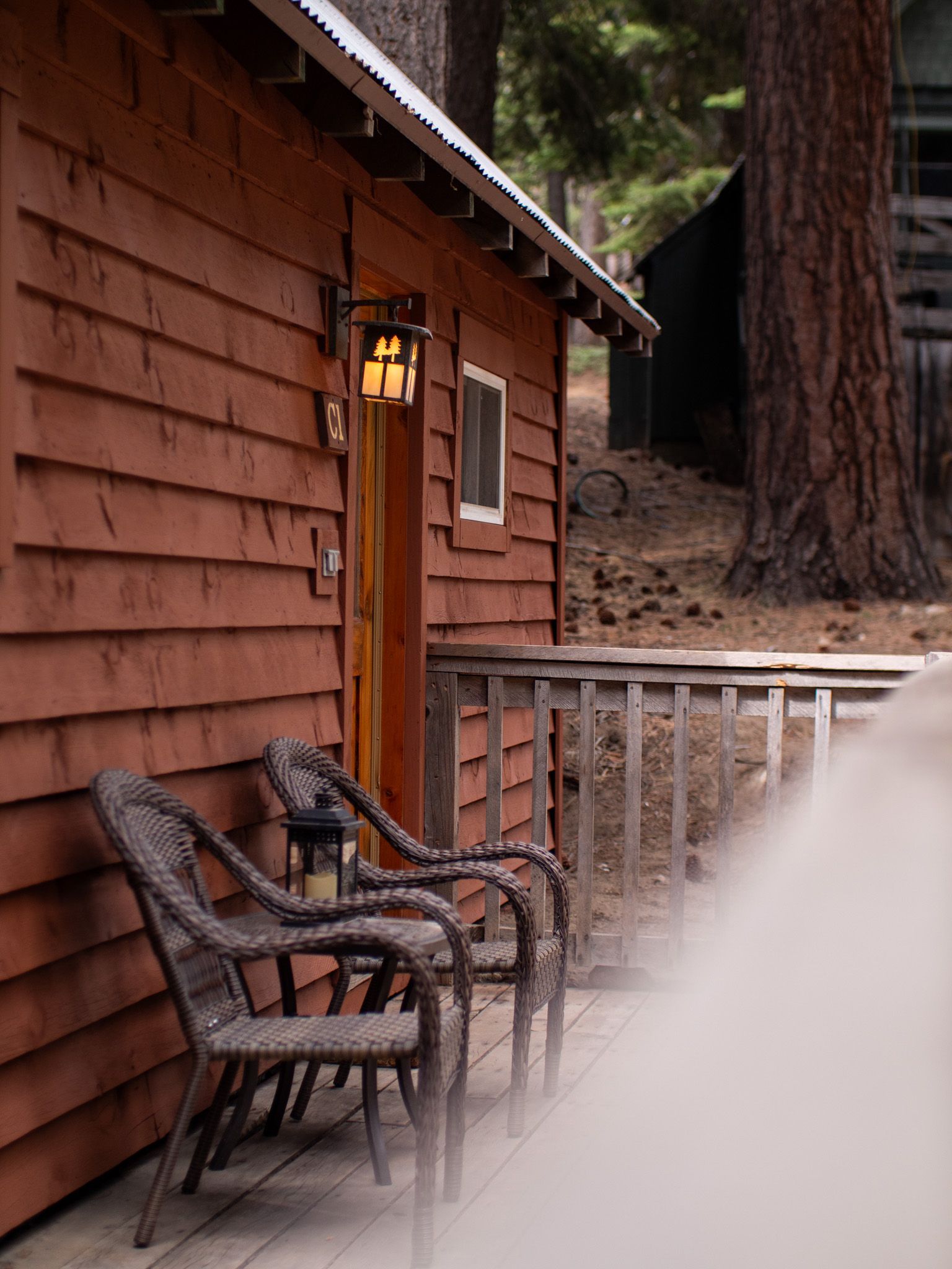 Cabin porch with two black chairs beside a wooden door and railing in a forested setting
