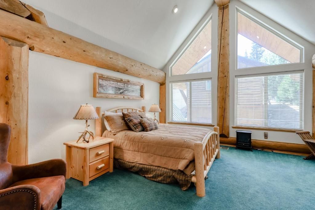 Bright attic bedroom with a bed, nightstand, teal carpet, and large triangular windows.