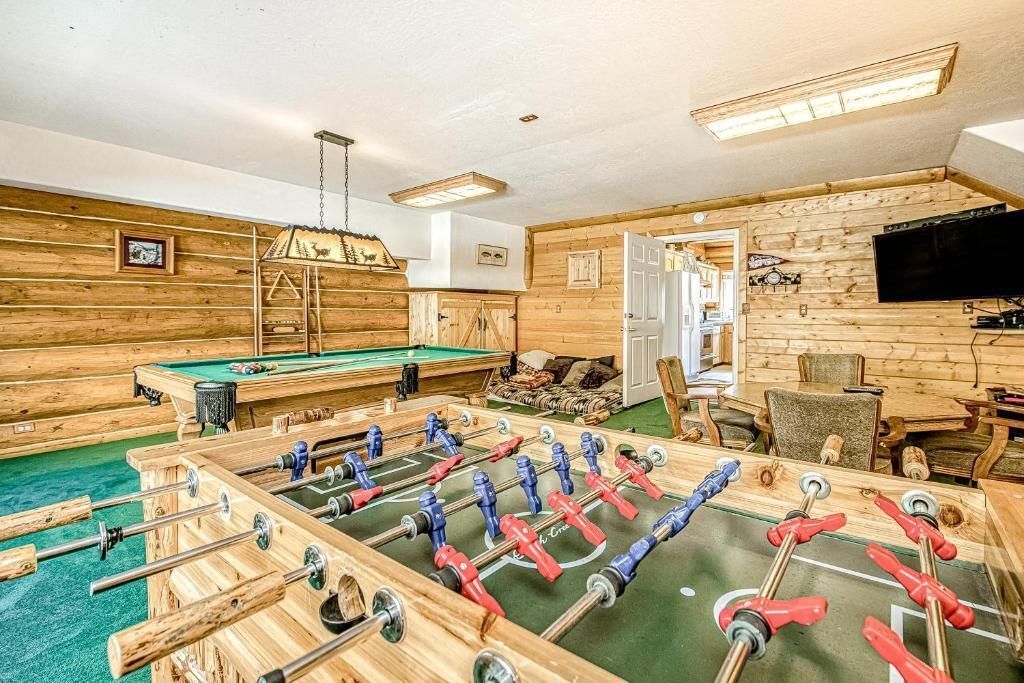 Foosball tables in a wood-paneled game room with wall-mounted TVs and ceiling lights