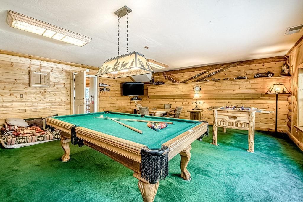 Pool table in a basement recreation room with green carpet, wood-paneled walls, and overhead lights