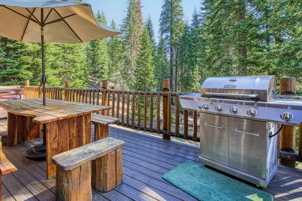 Wooden deck with outdoor dining table, umbrella, grill, and forest view in sunlight