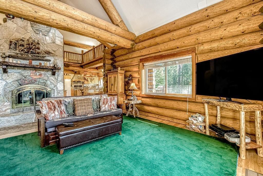 Rustic log cabin living room with green carpet, fireplace, sofa, window, and wall-mounted TV