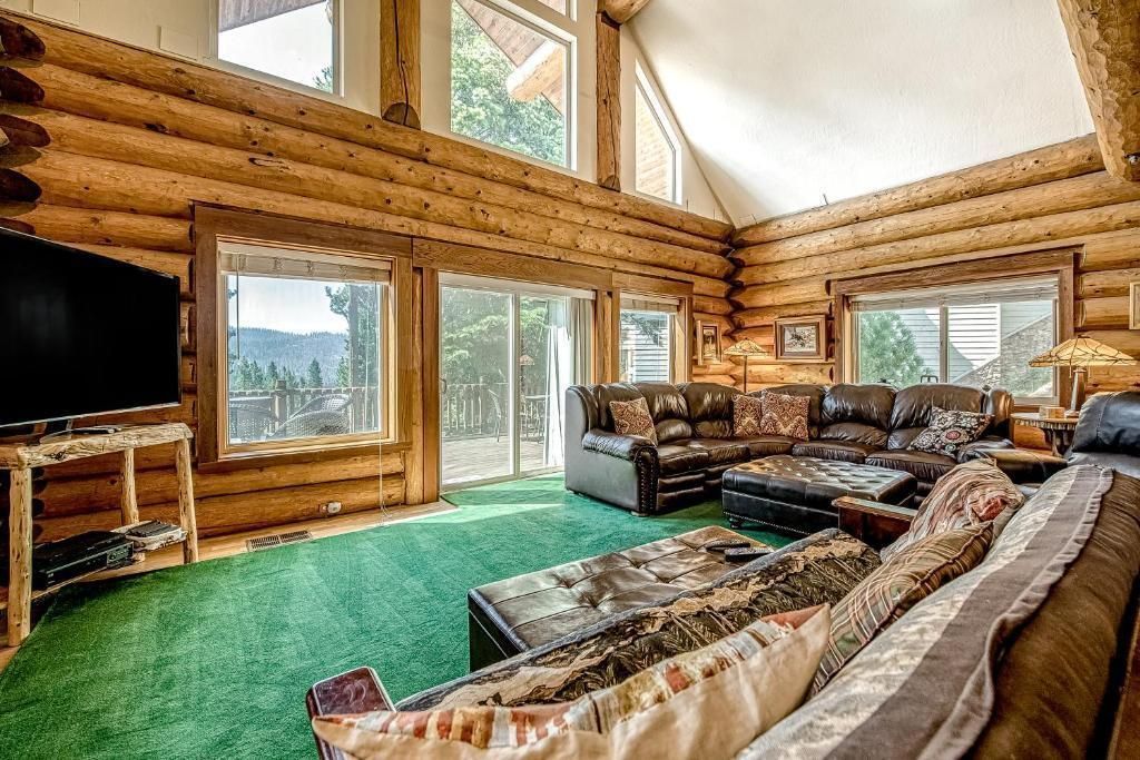 Log cabin living room with leather sofas, green carpet, large windows, and mountain views