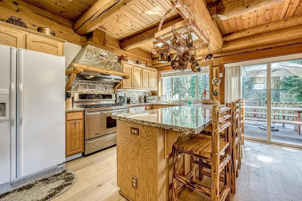Rustic kitchen with wood beams, white fridge, island chairs, and sliding glass doors to a snowy view
