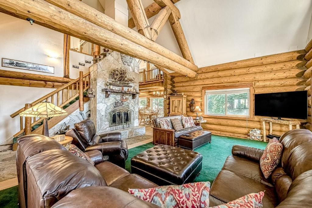Rustic log cabin living room with leather sofas, stone fireplace, green rug, and large windows