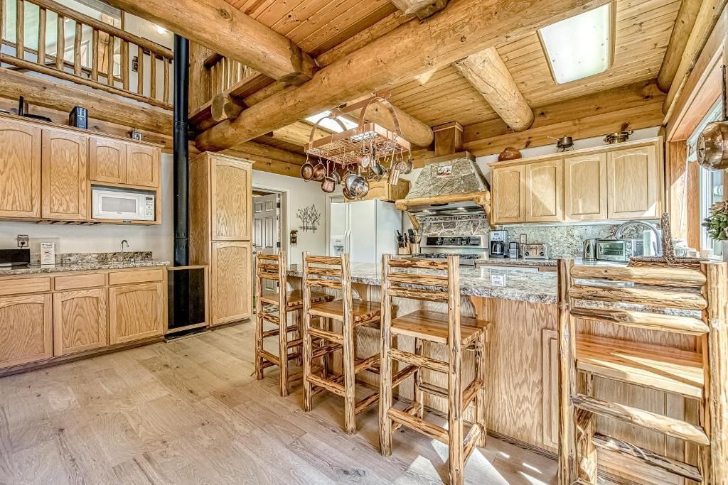 Rustic log cabin kitchen with wood cabinetry, dining table, and wooden chairs under exposed beams