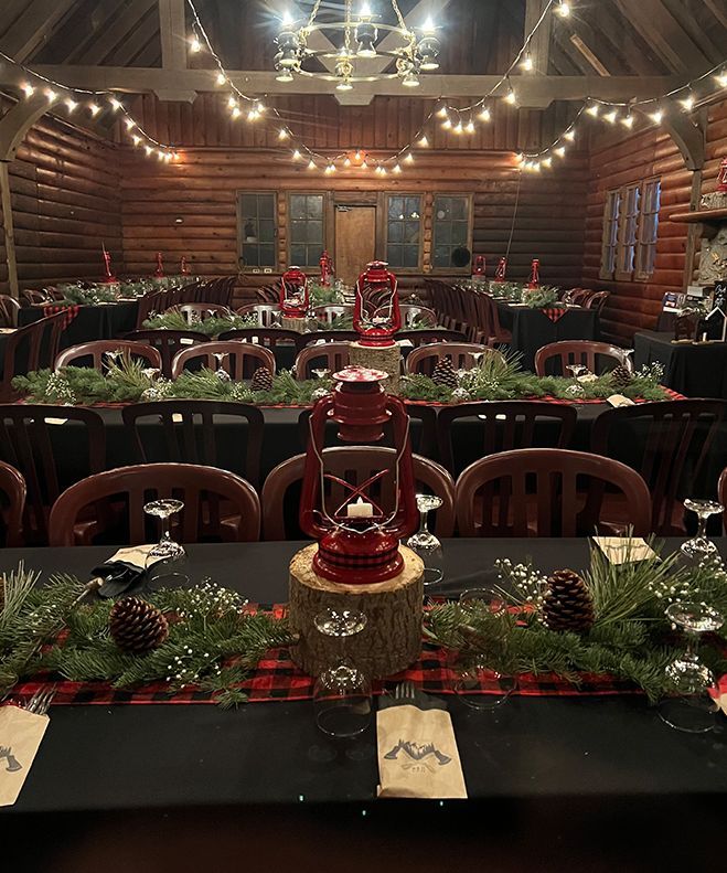 Formal dinner table setting with red lanterns, greenery, and plaid runner in a wooden cabin.