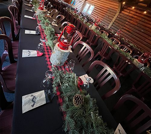Long dining table set for a holiday meal, decorated with greenery and red accents.