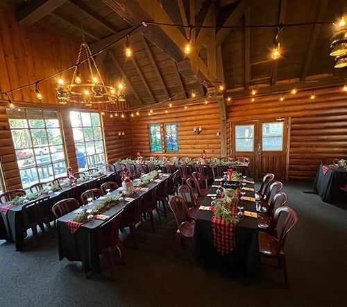 Wedding reception in a log cabin with tables set for guests, string lights, and a chandelier.