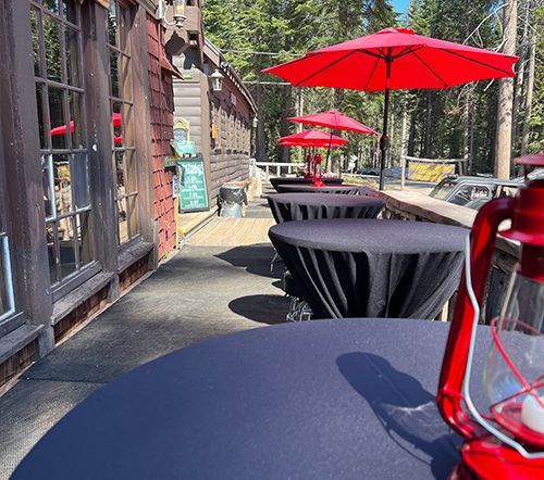 Outdoor dining area with black tablecloths, red umbrellas, and a red lantern.
