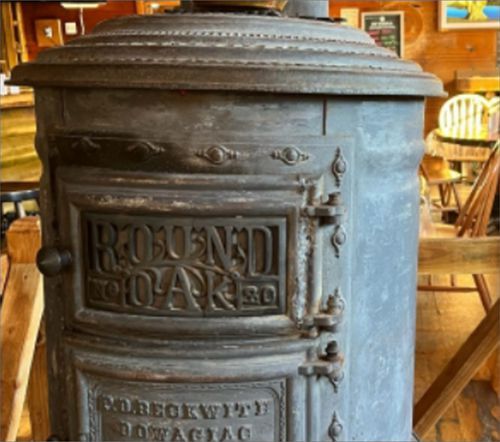 Antique, cast iron Round Oak stove. Gray metal with embossed lettering, handles, and a round top.
