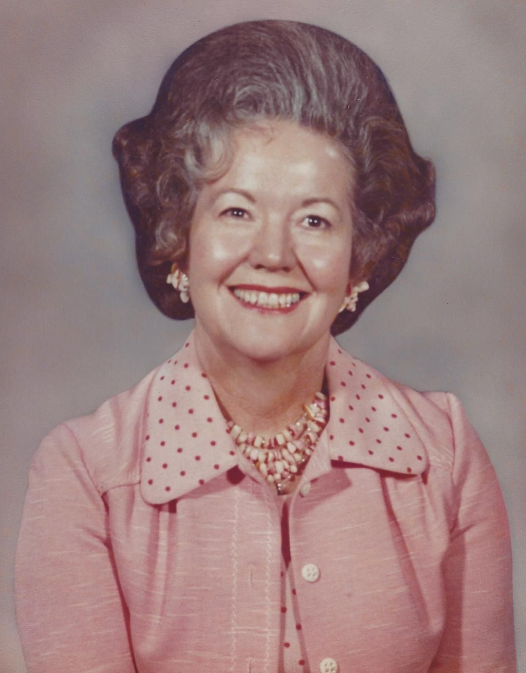 Smiling woman in a pink blouse with a polka-dot collar, posing for a studio portrait.