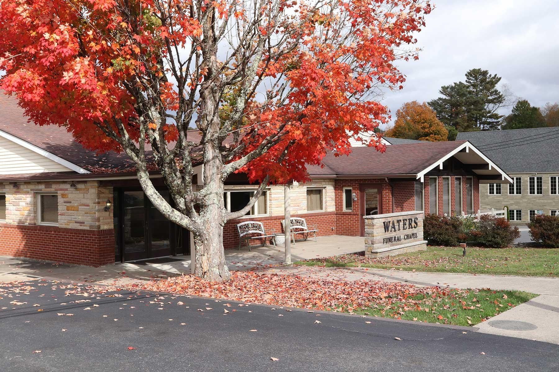 Single-story brick building with red autumn tree and a parking lot in front