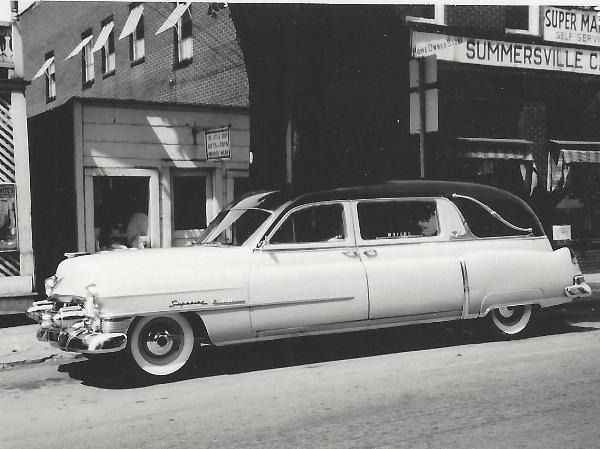 Classic white vintage car parked on a city street in front of storefronts.