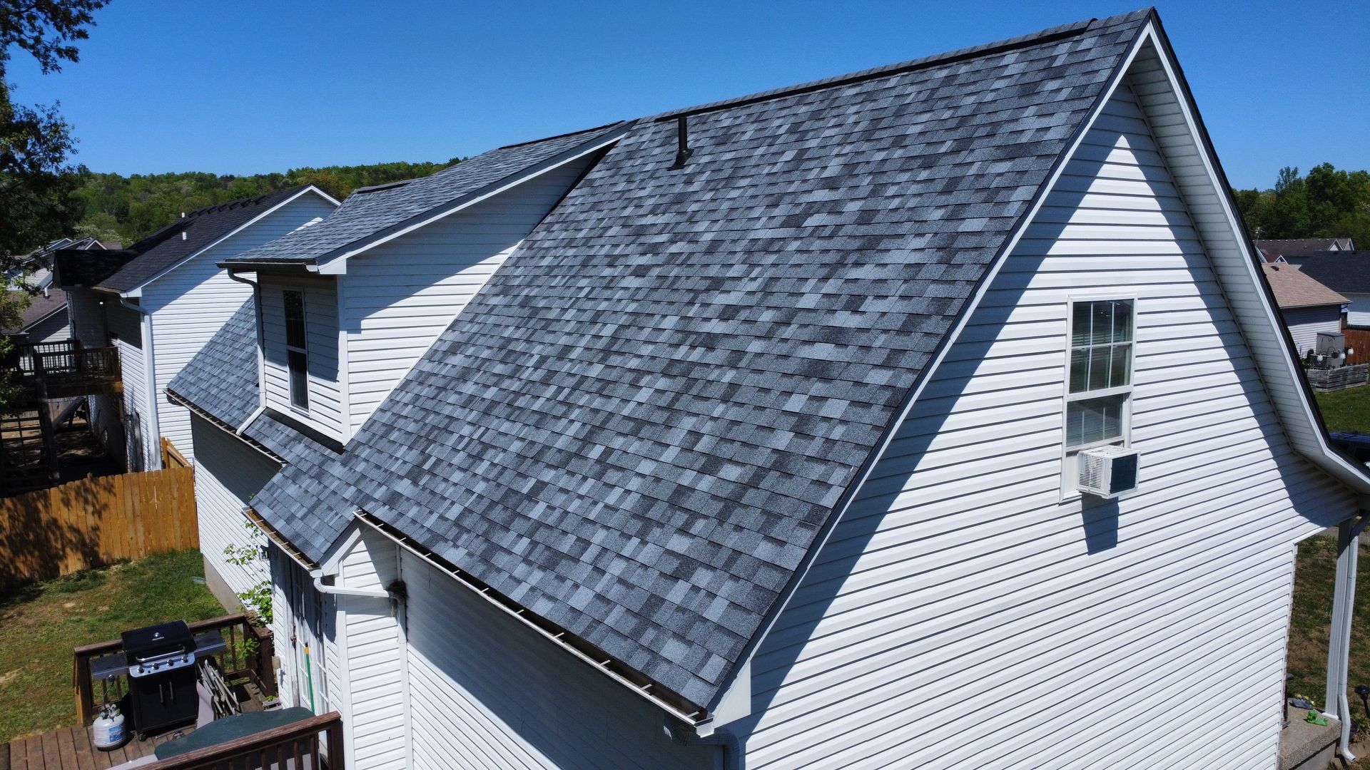 Gray shingled house roof with white siding and a small dormer under a clear blue sky