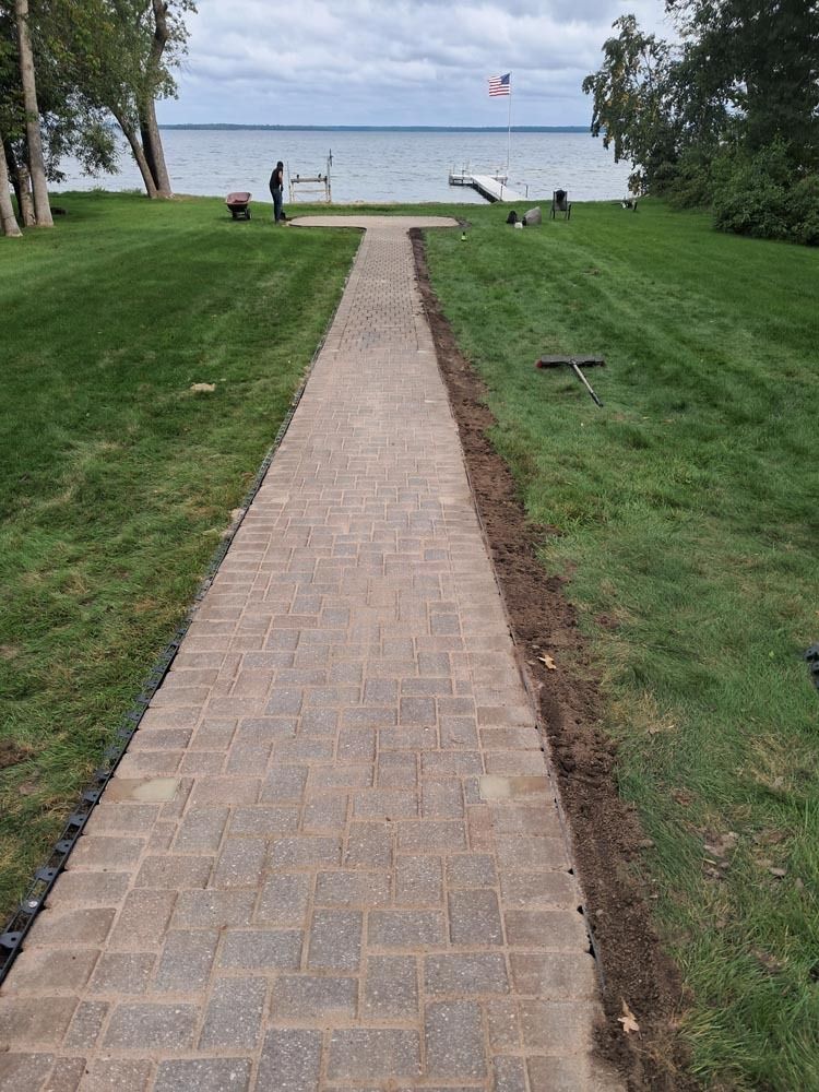 Brick path through grassy park to a lake with a bench and an American flag in the distance