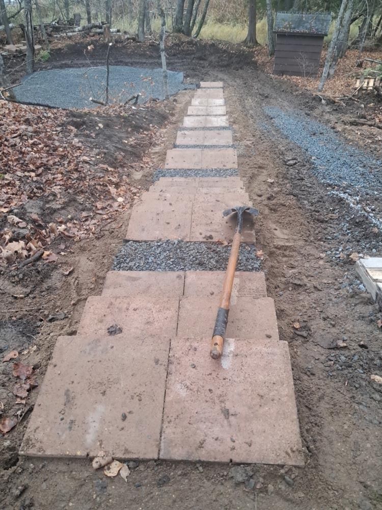 Wooden plank walkway under construction in a muddy garden with a shovel lying on it
