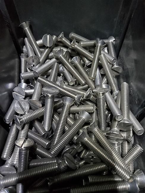 Un montón de tornillos de acero inoxidable en un recipiente de plástico.