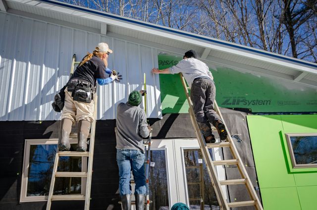 Three workers on ladders painting a building exterior white and green.