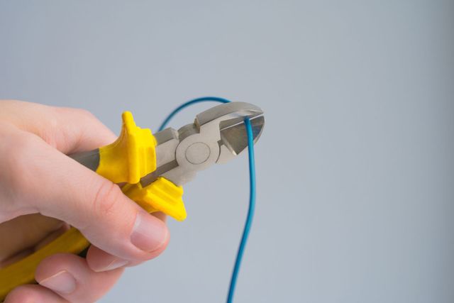 Hand using pliers to cut a blue wire against a light gray background