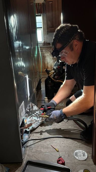 Technician in safety glasses and gloves working on exposed wiring inside a narrow hallway.