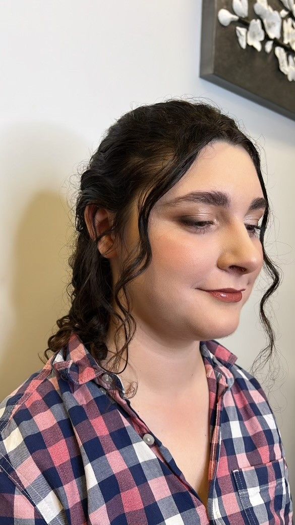 A woman with professional makeup and in a plaid shirt is standing in front of a wall.