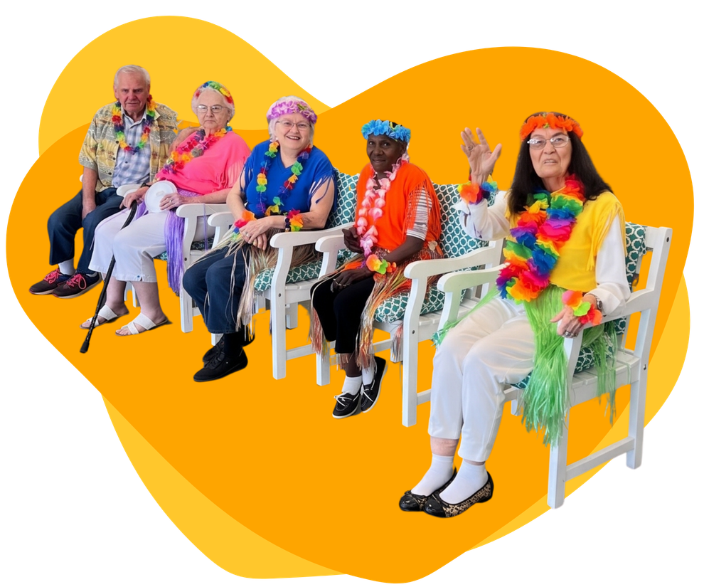 Five people in colorful leis sit on white chairs against a bright orange heart-shaped background.
