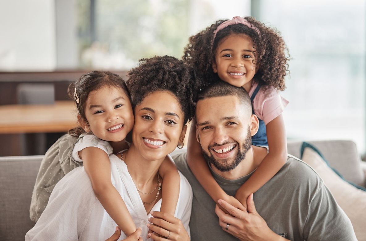 Smiling family of four hugging on a couch in a bright living room