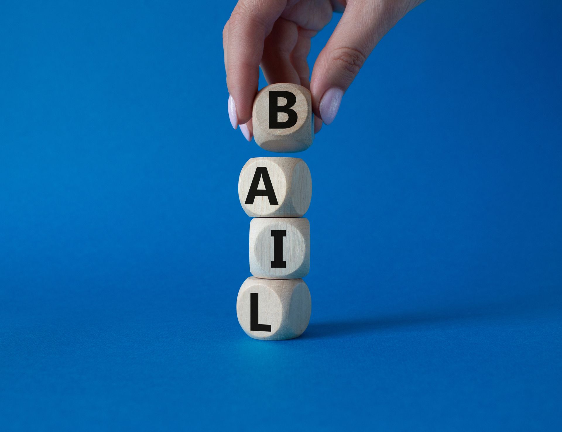 Hand stacking lettered blocks spelling BAIL on a blue background